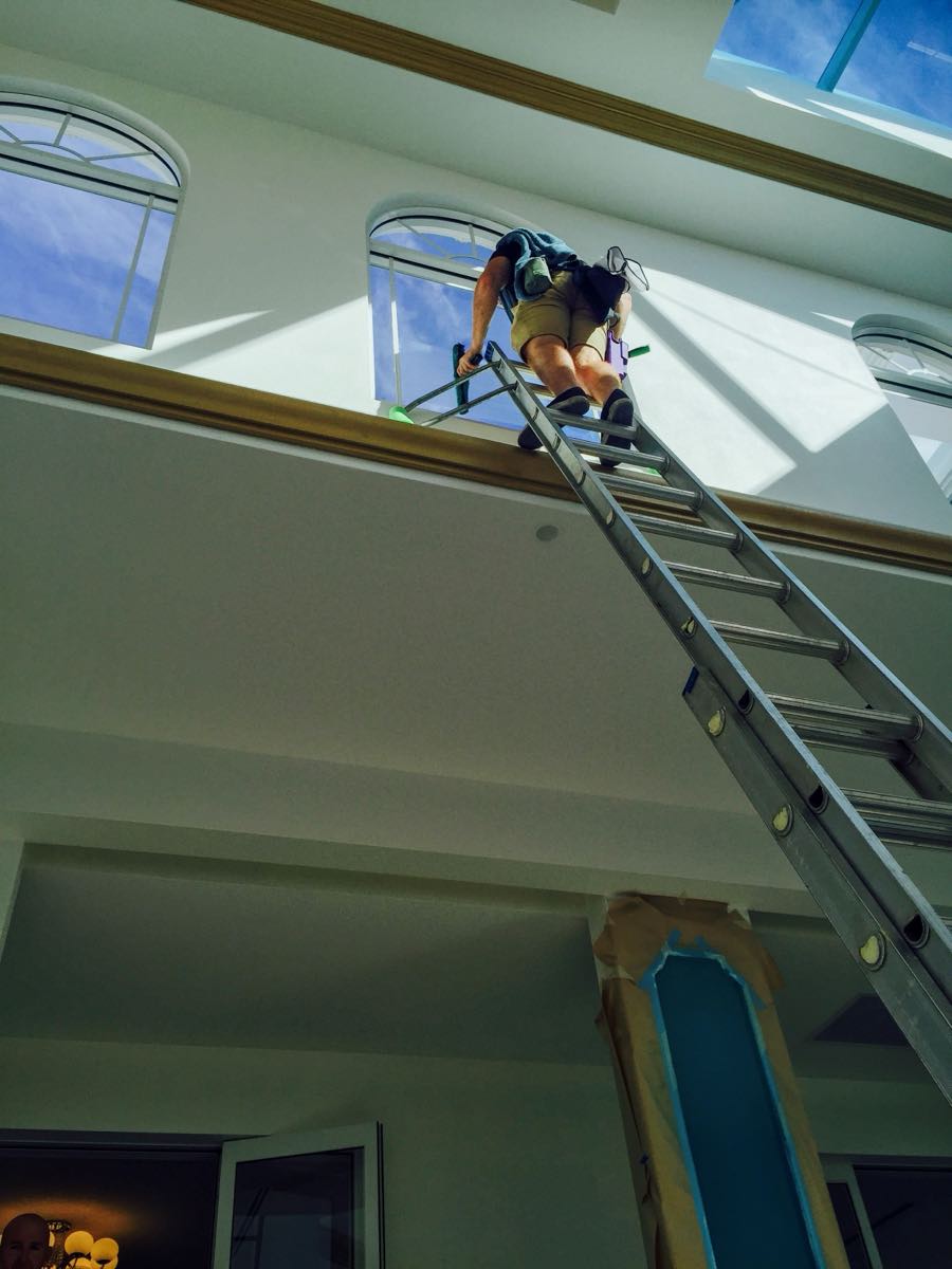 Rhys at the top of an extension ladder cleaning a high arched interior window on a Gold Coast job, Streakers era