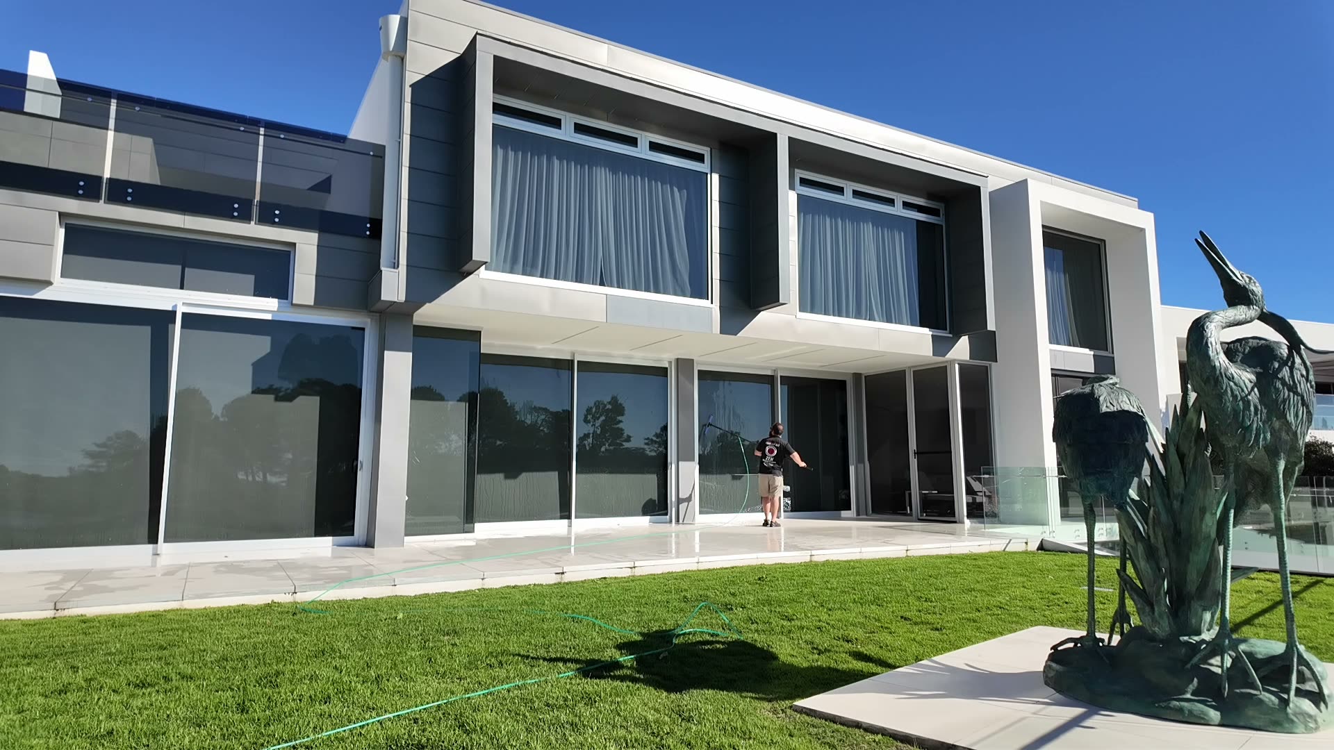 Rhys cleaning floor-to-ceiling windows in a Gold Coast beachfront property - direct ocean views and Zen-branded shirt visible