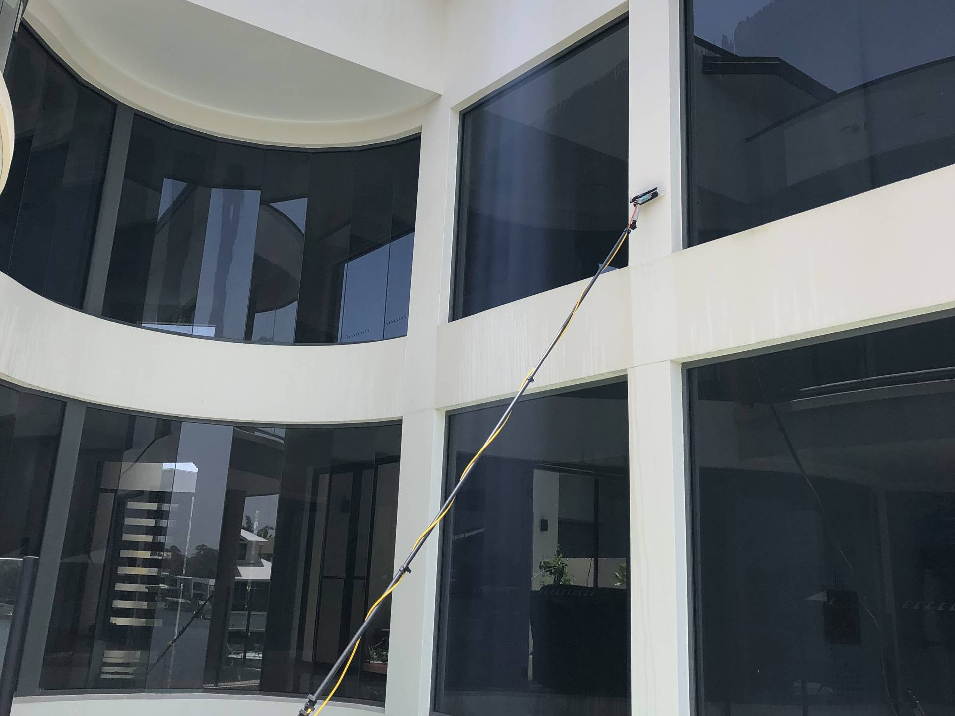 Water-fed pole cleaning the curved glass atrium of a Helensvale home