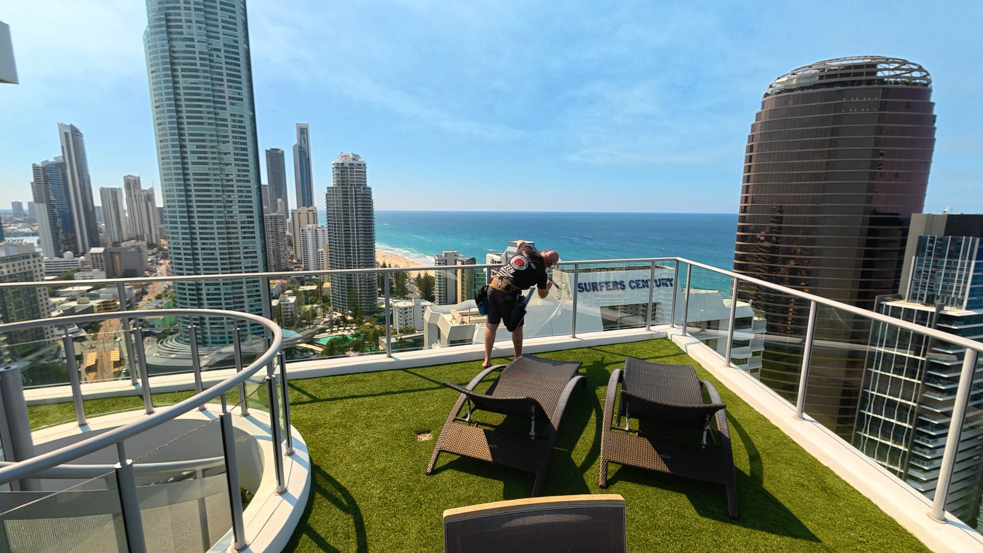Rhys cleaning the glass balustrade on a Surfers Paradise rooftop terrace, with the beach and towers behind
