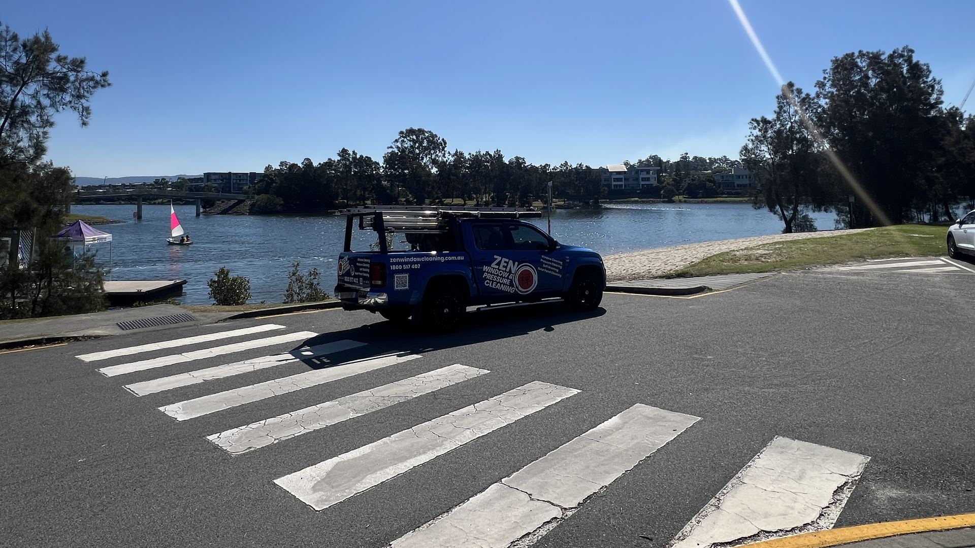 Zen Window Cleaning ute by the lake at Varsity Lakes with a sailing boat on the water